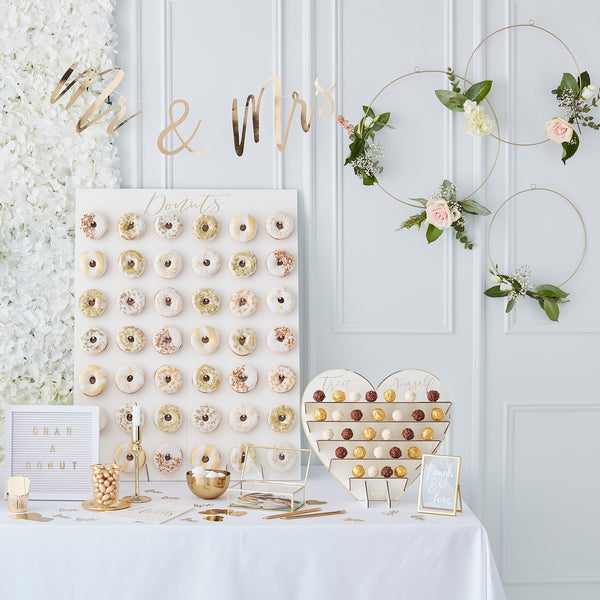 A range of gold and white themed items grouped together showing a lovely sweet table with donut rings, and message box