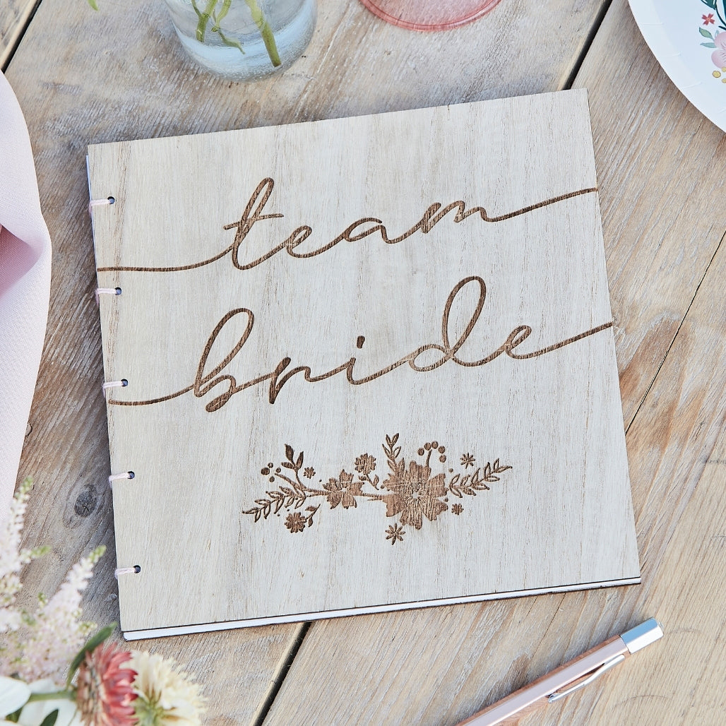 Wooden Team Bride Guestbook for Hen parties or Bridal Showers, the Book has wooden covers and bound with pink ribbon, it has the words "Team Bride" and a flower element engraved on the front cover.